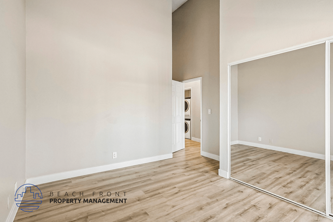 A room with wooden flooring and a white wall with a doorway leading to another room.